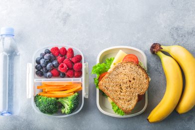 School lunch box with sandwich vegetables water almonds and fruits on black chalkboard